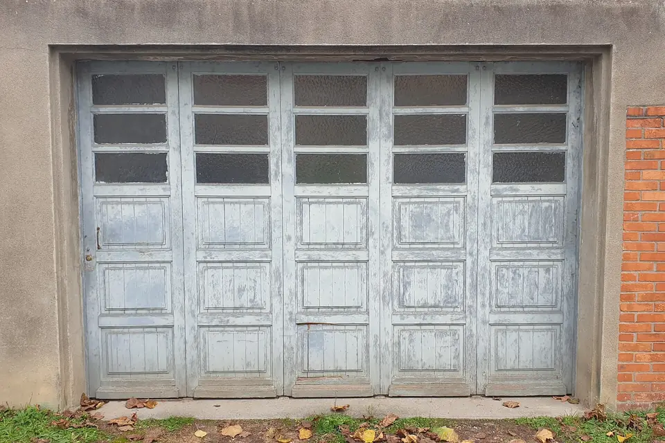 Porte de garage en bois peint à plusieurs vantaux, avec une rangée de vitres en partie haute, dans une façade enduite de Cusset.