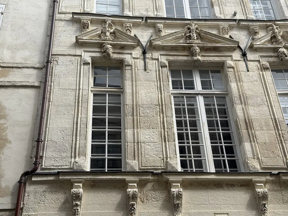 Façade en pierre d'une maison de la rue des Merciers à La Rochelle, avec hautes fenêtres à petits carreaux sous des frontons sculptés.
