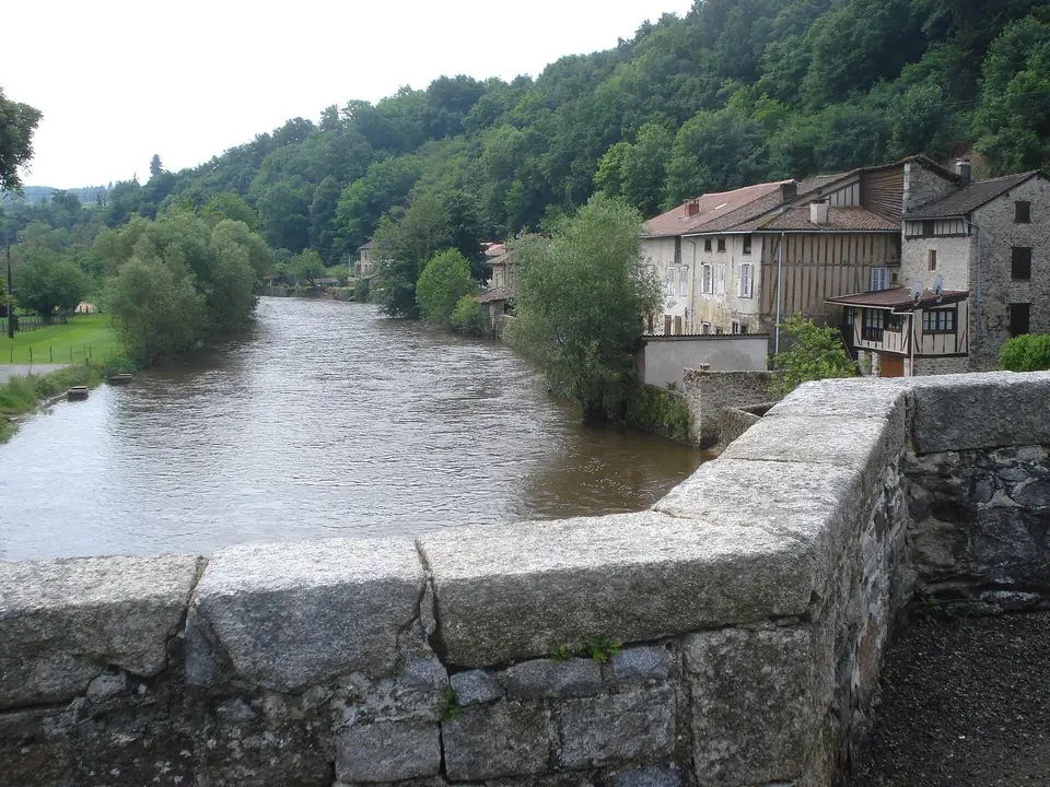 La Vienne à Pont-de-Noblat, au pied de Saint-Léonard-de-Noblat, bordée de maisons en pierre et à pans de bois sous une colline boisée.